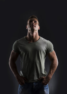 Handsome muscular fit young man on dark background looking up