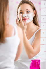 Young cute girl putting facial mask on her face