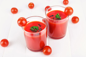 Tomato juice in glasses and fresh tomatoes on wooden background
