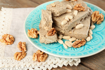 Sunflower halva with nuts on plate, on wooden background