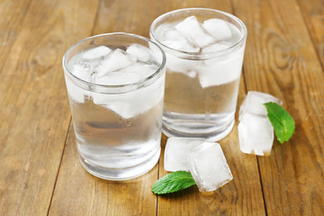 Glass of water with ice cubes on wooden table