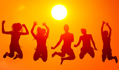 Silhouettes of teenage boys and girls jumping high in the air on sunny summer day