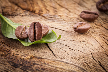 Coffee grains and green leaf on grunge wooden background