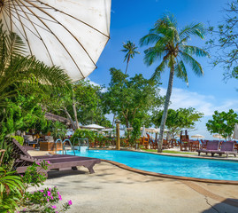White sun umbrella at azure swimming pool with wooden sunbeds