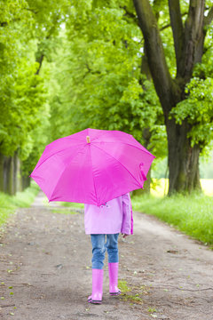 little girl wearing rubber boots with umbrella in spring alley