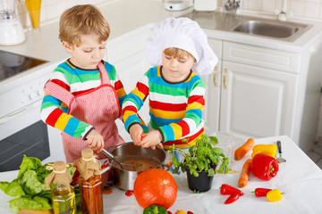 Little twins cooking italian soup and meal with fresh vegetables