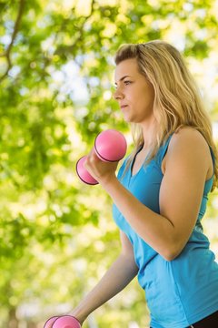 Fit blonde lifting dumbbells in the park