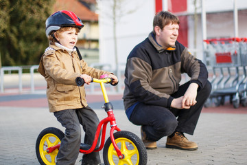 Little toddler boy with bicycle and his father in the city