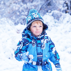 Adorable toddler boy having fun with snow on winter day