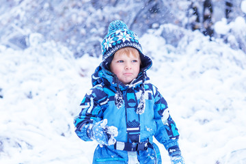 Adorable toddler boy having fun with snow on winter day