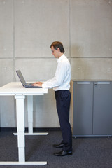 Businessman with eyeglasses standing at  height adjustment table