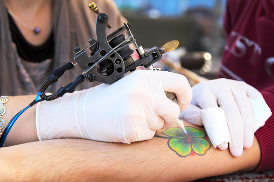tattooer showing process of making a tattoo.  four-leaf clover