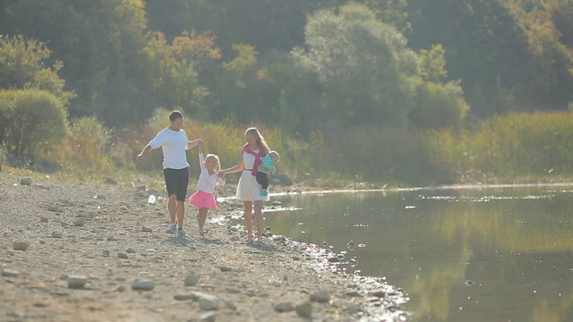 Happy family with two kids walking along the shore of the pond