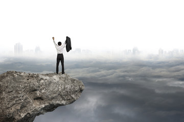 man cheering on cliff with gray cloudy sky cityscape background