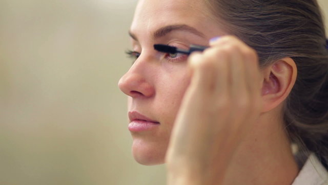 Young beautiful woman applying makeup on eyelid with brush