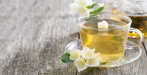 Obraz na płótnie Canvas Glass cup of green tea with jasmine on wooden background