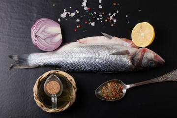 Fresh sea fish lying on dark background with spices.
