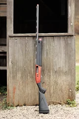 Foto auf Acrylglas Antireflex Modern shotgun leaning against a wood cabin © indiauniform