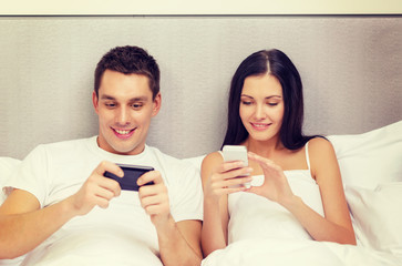 smiling couple in bed with smartphones