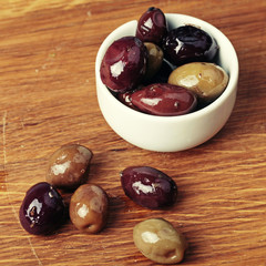different olives in white bowl on wooden board