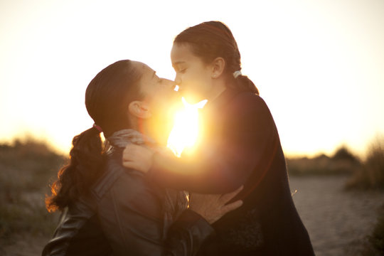 Madre e hija d&aacute;ndose un beso en contraluz