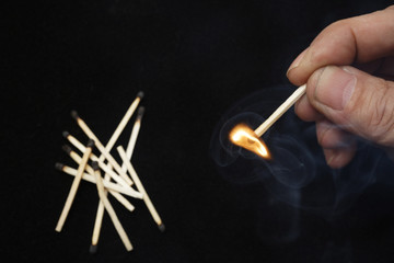 Hand holding burning match stick on black background
