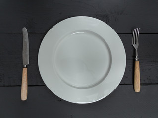 Besteck und Teller auf schwarzem Holzhintergrund