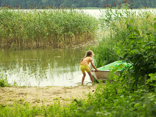 little girl playing with boat by a river on summer day