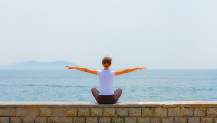 Fototapeta na wymiar Girl sitting at seaside and exercise yoga, woman fitness