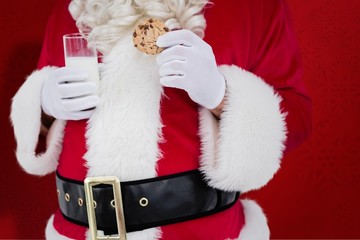 Composite image of santa holding cookie and glass of milk