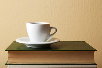 Cup of hot drink on book on light wall background