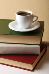 Pile of books with cup on tabletop and light wall background