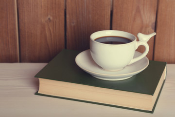 Cup of hot drink on book on tabletop and wooden background
