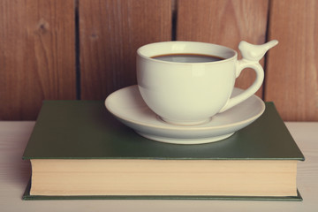 Cup of hot drink on book on tabletop and wooden background