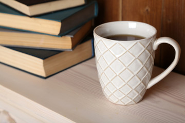 Pile of books with cup on tabletop and wooden background