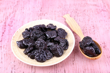 Bowl and spoon of prunes on color wooden background