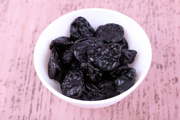 Bowl with heap of prunes on color wooden background
