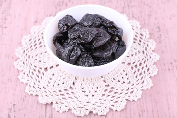 Prunes in bowl on lace doily on color wooden background