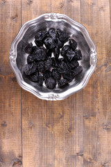 Metal plate of prunes on wooden background