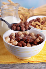 Various sweet cereals in ceramic bowl, fruits and jug with milk