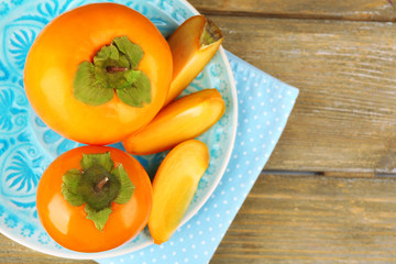 Ripe persimmons on plate, on wooden background