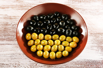 Black and green olives in bowl on painted wooden background
