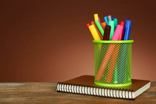 Colorful markers in green metal holder with notebook