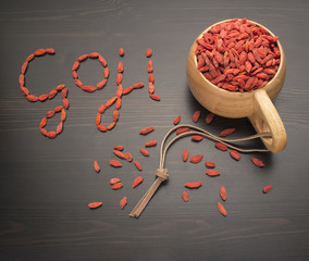 Caption goji berries on a black table, next to a cup filled