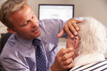 Doctor Fitting Senior Female Patient With Hearing Aid - Powered by Adobe