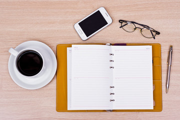 a table with notebook, smartphone, eye glasses, and pen