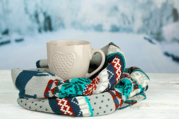 Cup of hot drink with warm scarf on table