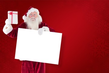 Composite image of santa shows a present while holding sign