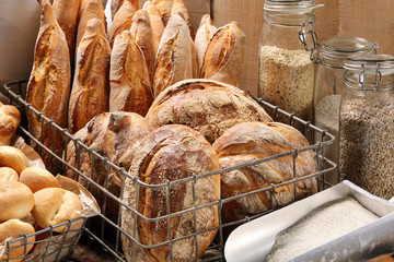 Fresh bread in metal basket in bakery on wooden background