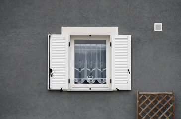 Fototapeta na wymiar Holzfenster mit weißem PVC Klappladen in grauer Fassade